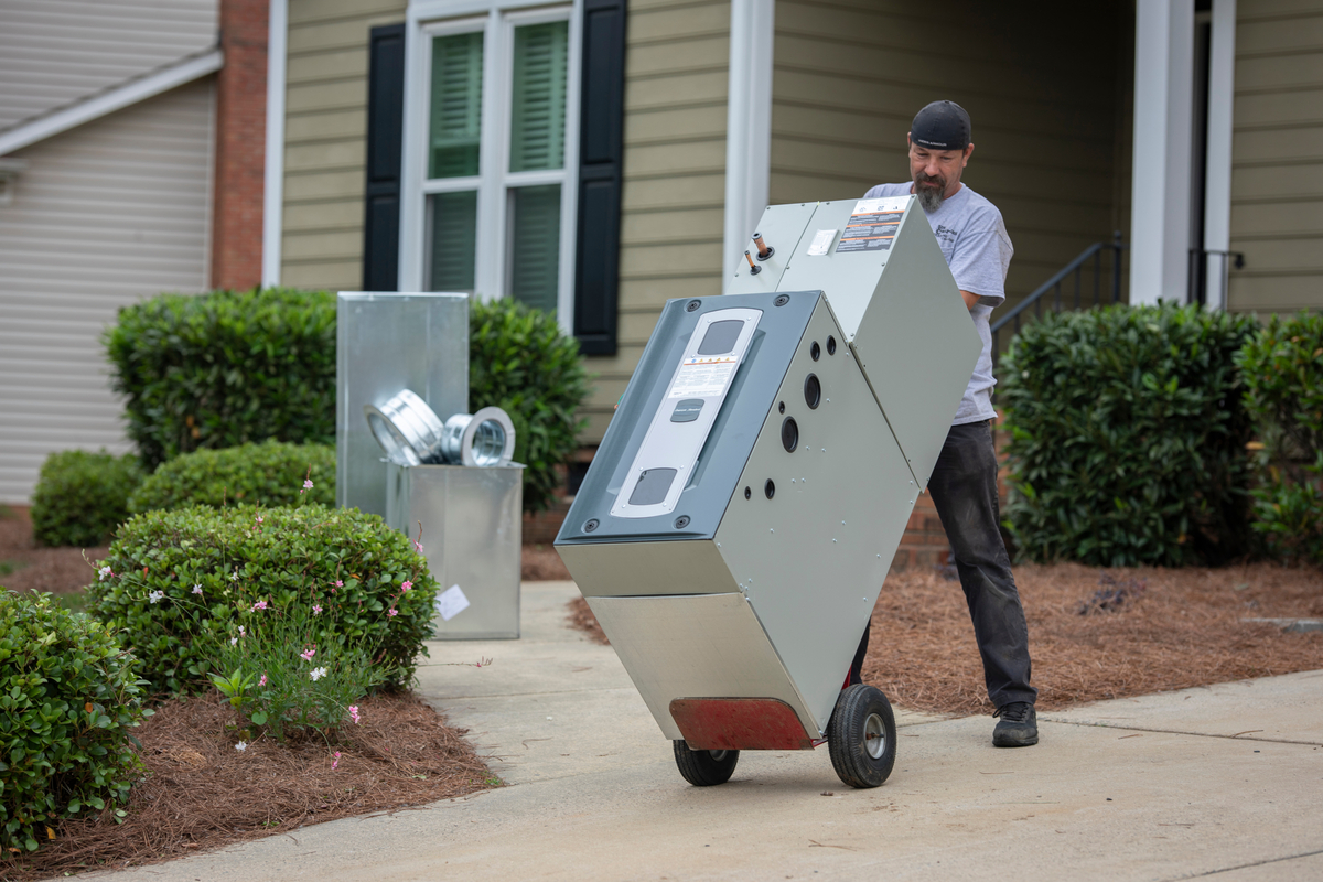 Technician moving an HVAC unit on a hand truck up front steps