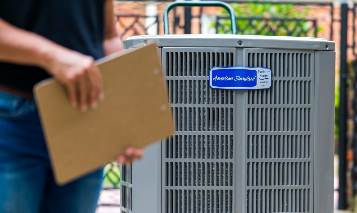 Hand holding an HVAC air filter in front of an outdoor AC unit