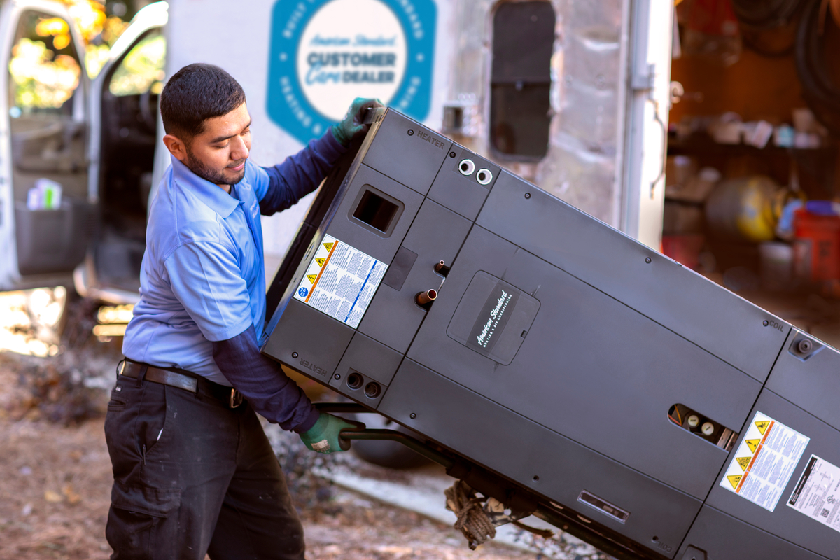 HVAC technician carrying an outdoor condenser unit